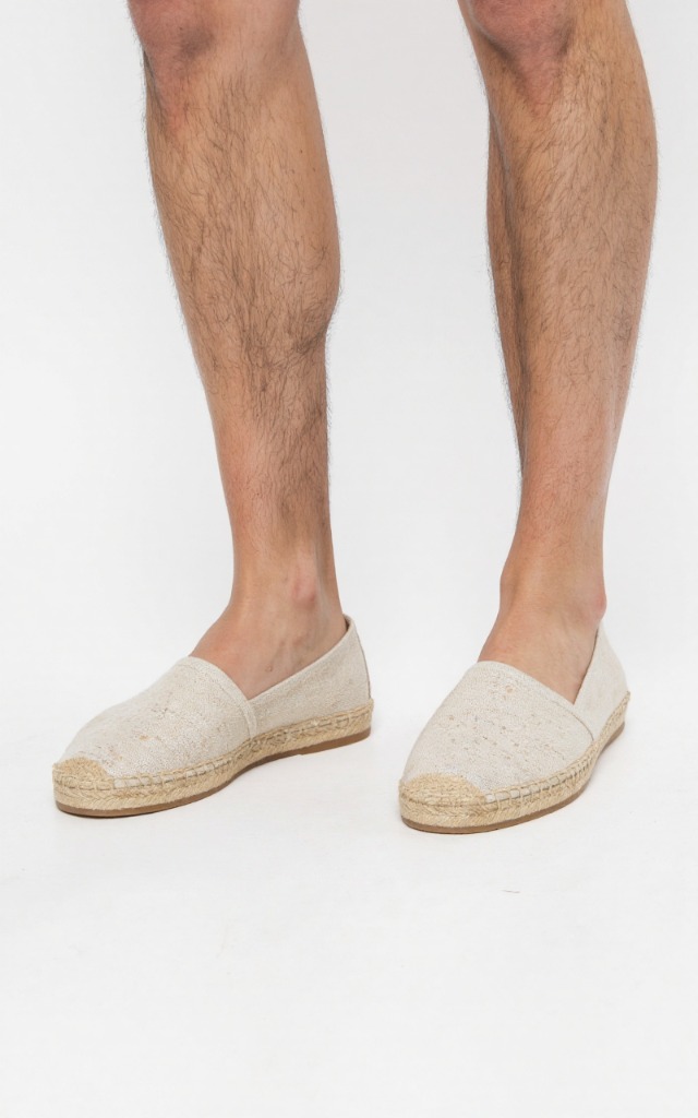 A male model wearing Espadrilles with canvas uppers, against a white background, with a close   up of the feet